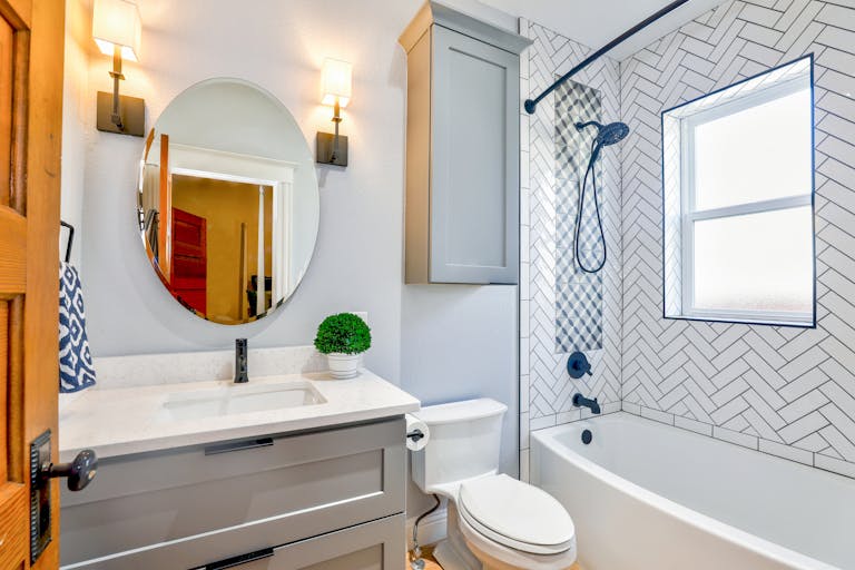 Elegant Modern Bathroom Featuring Chevron Tiles, Oval Mirror, And Sleek Fixtures For A Contemporary Look. Also Shown Is A New Plumbing Installation With A Toilet, Shower, And Sink